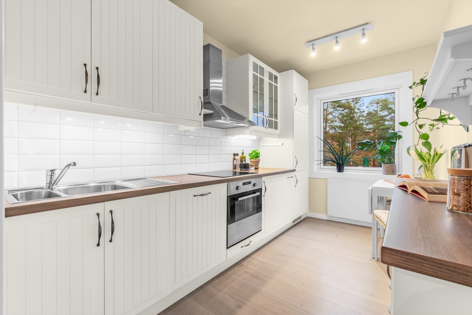 Kjøkkenet har innredning med profilerte fabrikklakkerte fronter, samt et vitrineskap, laminat benkeplate med nedfelt kum i rustfritt stål, lys under overskap og fliser på vegg over benkeplaten. Galleribilde