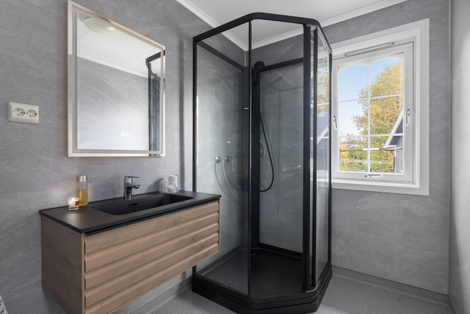 Stilrent bad fra 2024 med moderne innredning, dusjkabinett og baderomsplater i delikate gråtoner. Galleribilde