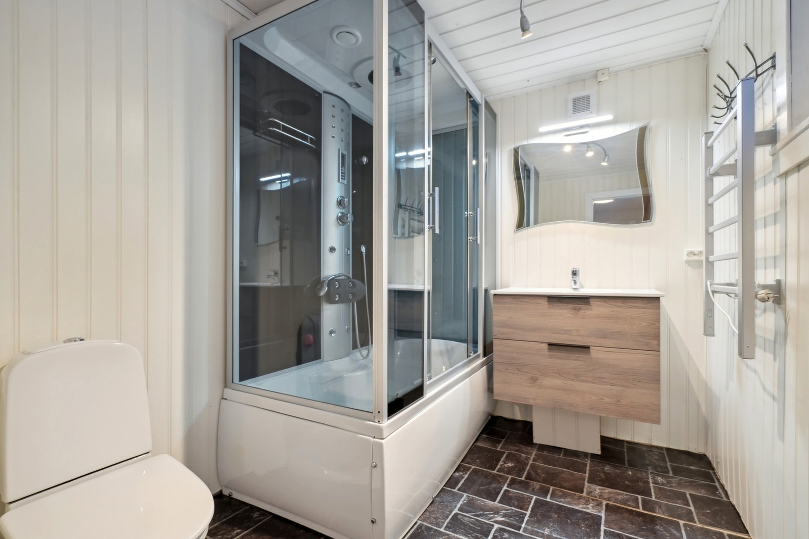 Badet i etasjen har flis og vinylbelegg på gulvet. Det er utstyrt med baderomsmøbel med skuffefronter og overliggende speil med belysning. Videre er det toalett og dusjkabinett. Galleribilde