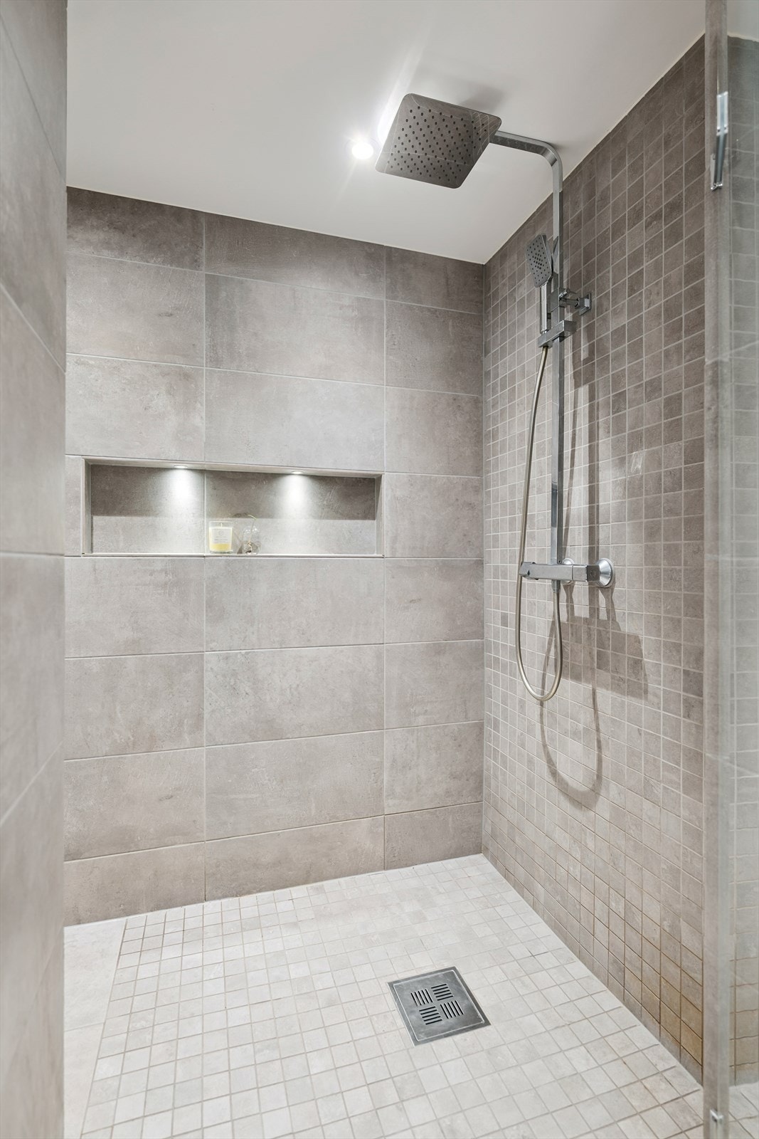 Badet er utstyrt med romslig dusjnisje med glassdør, vegghengt wc og servantinnredning med skuffer. Galleribilde