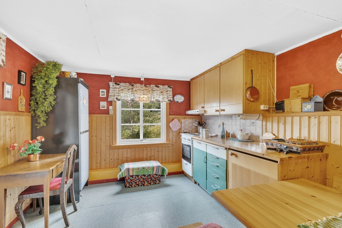 Kjøkkenet er innredet med glatte og profilerte fronter, frittstående komfyr, vaskemaskin og kjøleskap. Galleribilde