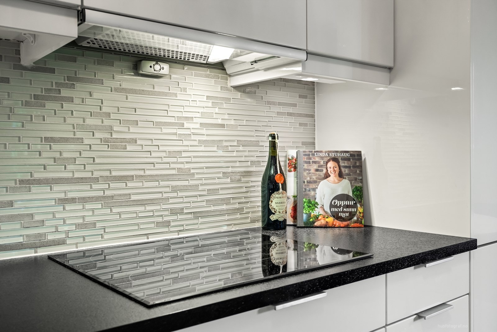 Hvite glatte høyglans fronter og benkeplate av laminat nedfelt en koketopp og en kompositt oppvaskkum. Galleribilde