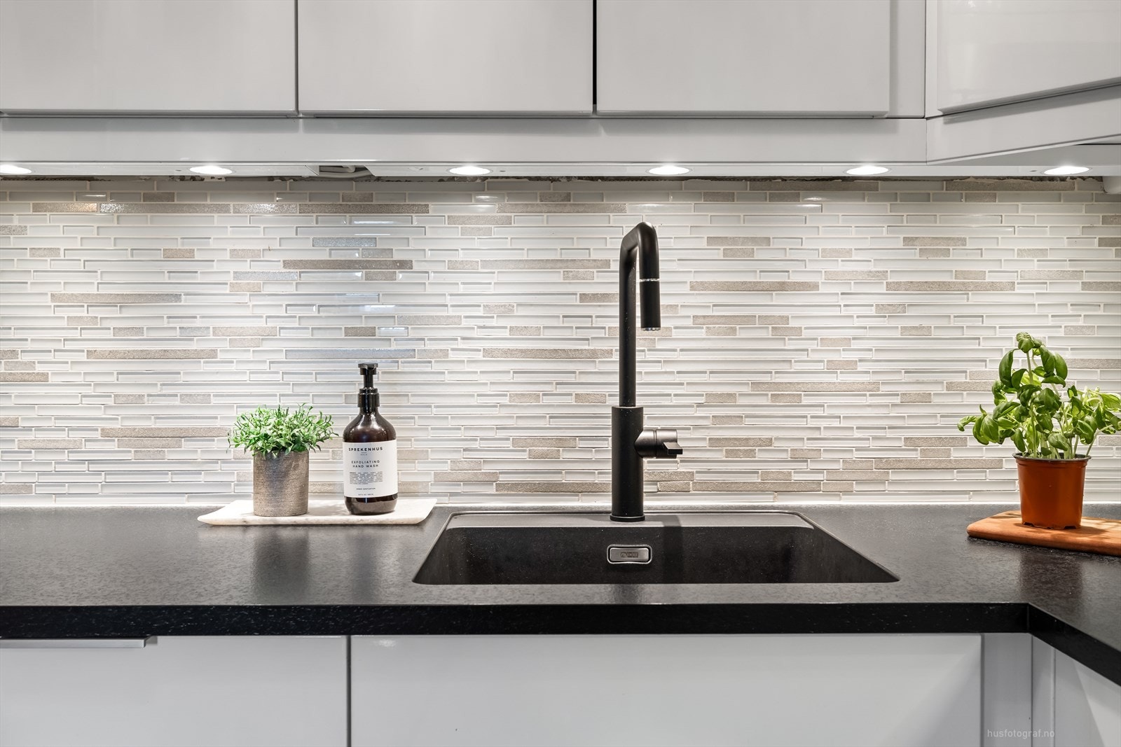 Kjøkkenet bærer et moderne preg med fliser over benkeplaten og pen belysning under overskap. Galleribilde