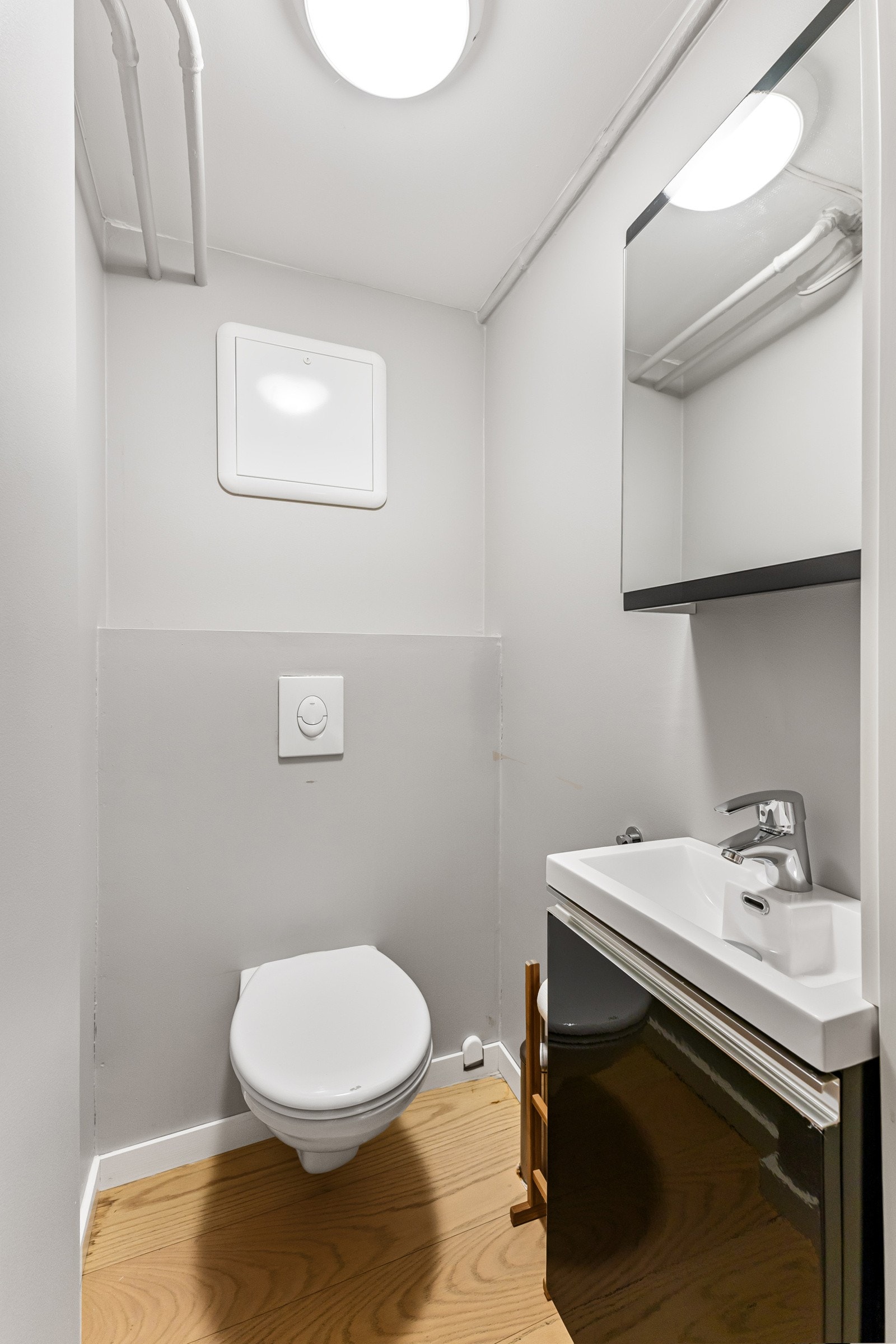 Det ene toalettrommet har inngang fra kjøkkenet, pent innredet med enstavs eikeparkett, gråmalte vegger og vegghengt toalett. I tillegg er det servantskap med sort høyglansfront, håndvask og et tilhørende speilskap med belysning. Galleribilde