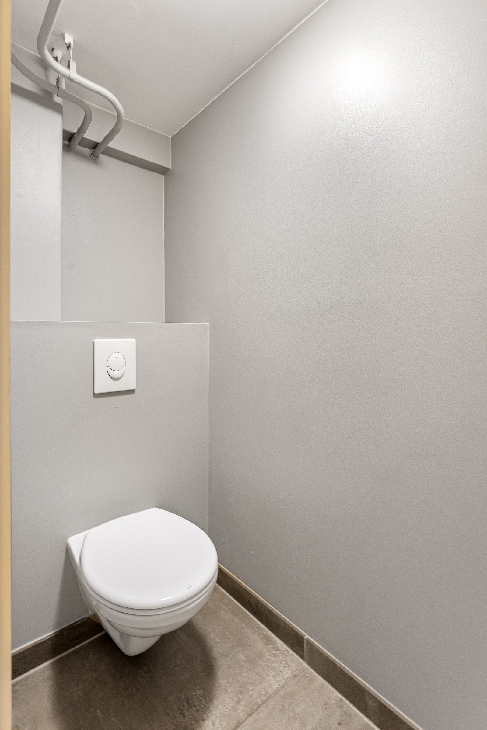 Det andre toalettrommet ligger i terskelfri tilknytning til badet. Rommet har store, grå fliser med sokkelflis, gråmalte vegger og et vegghengt toalett. Galleribilde