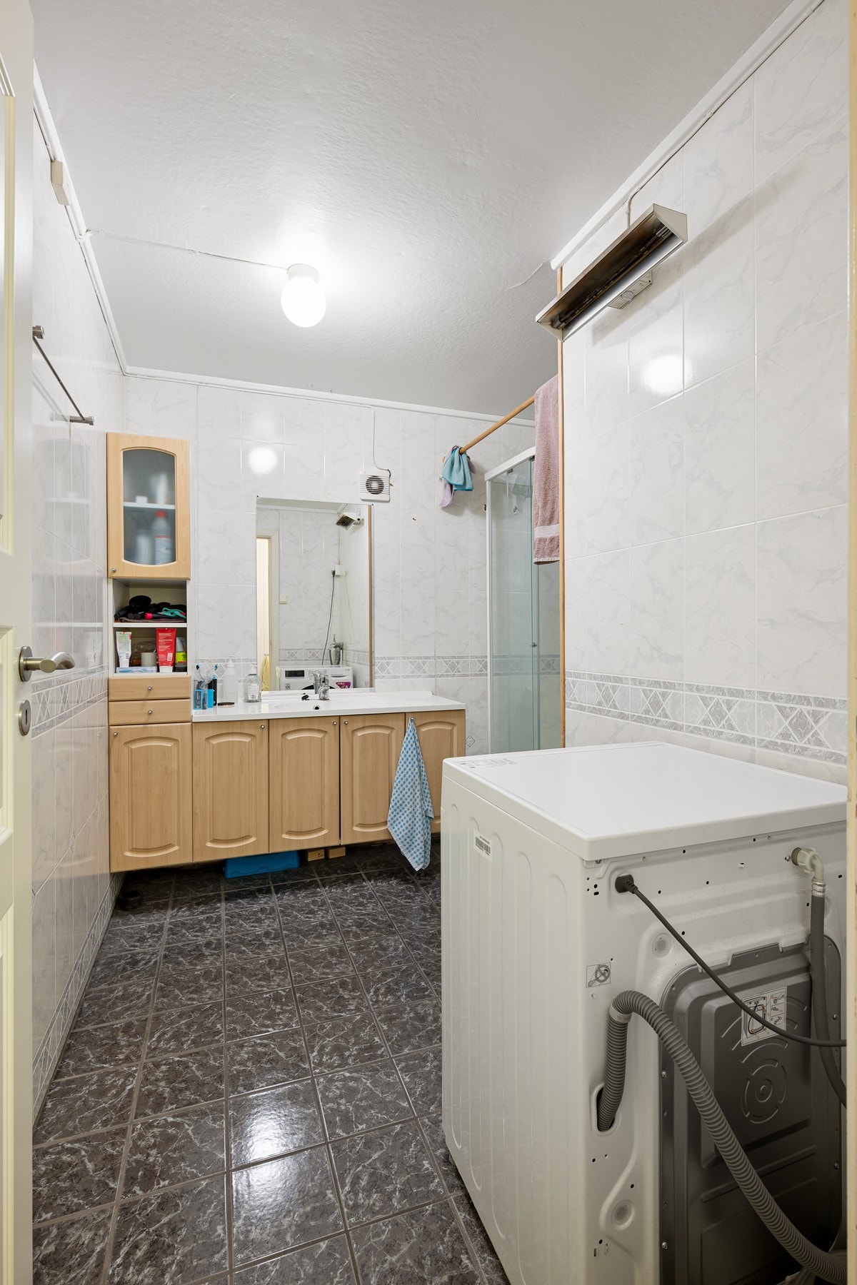 Flislagt bad/vaskerom med varme i gulv - inneholder dusjkabinett, servantinnredning og røropplegg til vaskemaskin Galleribilde