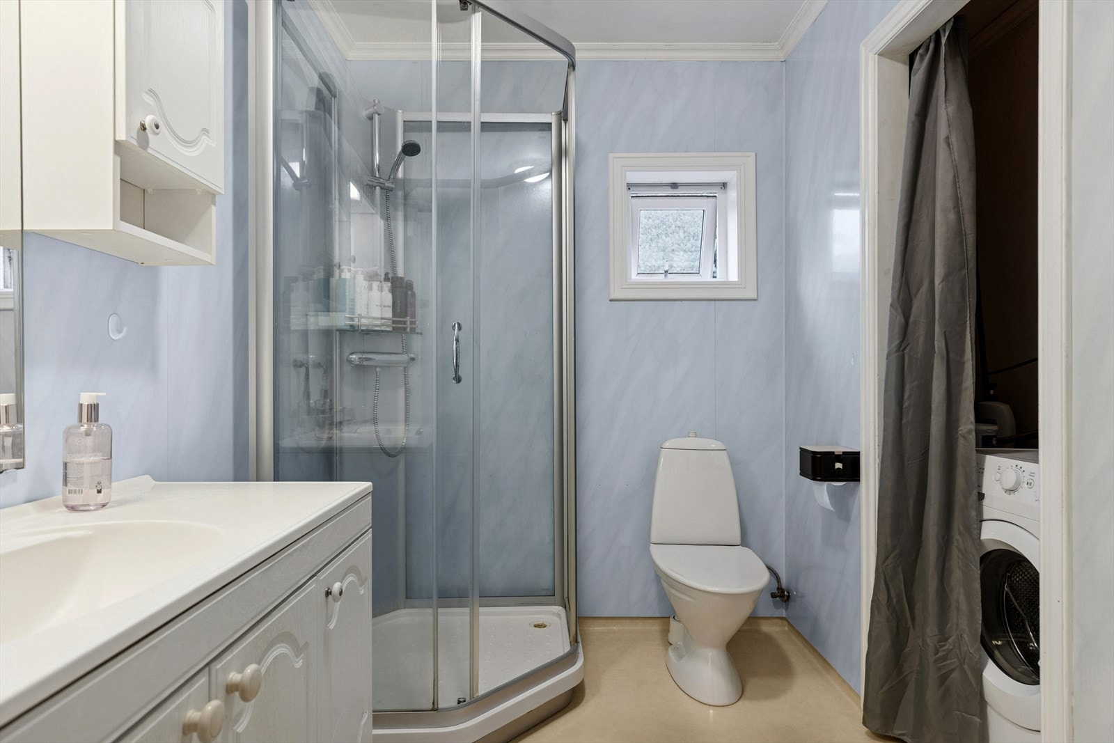 Kombinert bad og vaskerom med vinylbelegg på gulvet, baderomsplater på veggene og malte plater i taket. Galleribilde