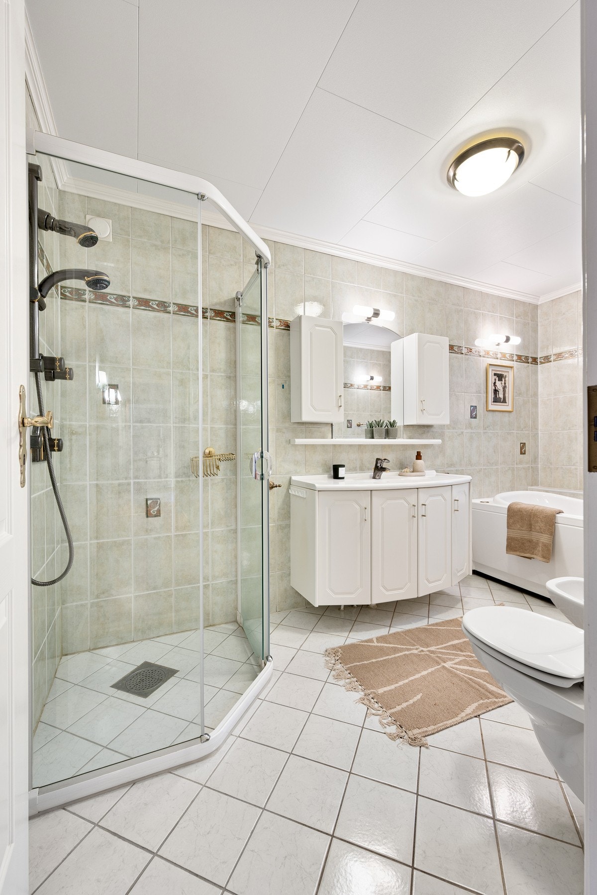 Flott flislagt bad med dusjhjørne, servantinnredning, badekar, toalett og bidé Galleribilde