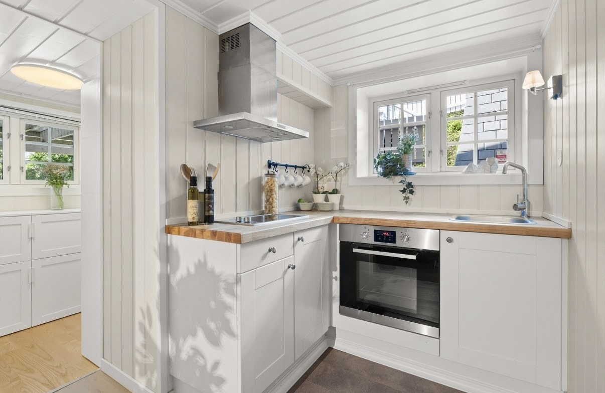 Lyst kjøkken med kokeplate, komfyr og kombi kjøle/fryse-skap. Galleribilde