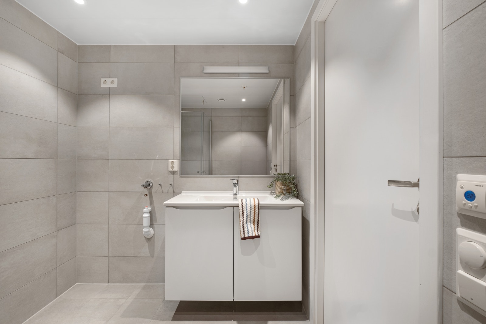 Badet er helfliset med moderne grå fliser som gir et stilrent preg, og gulvet er utstyrt med varmekabler for ekstra komfort. Galleribilde