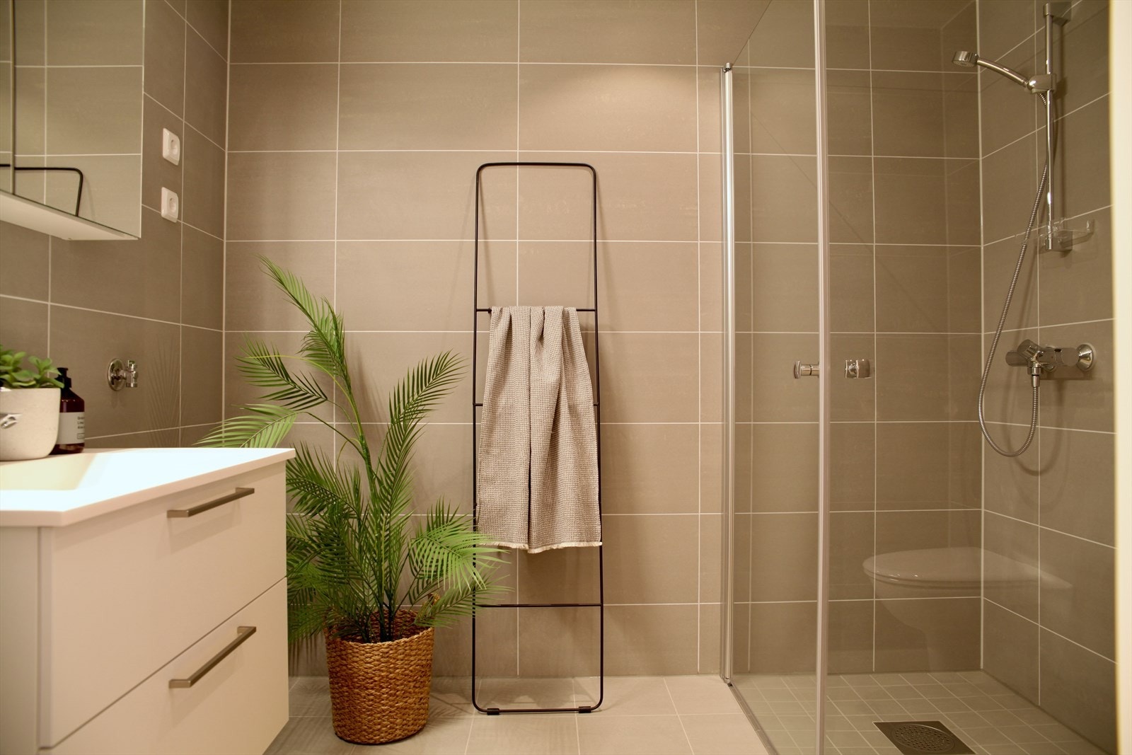 Et pent flislagt bad av god størrelse, utstyrt med dusjhjørne og vegghengt servant. Galleribilde