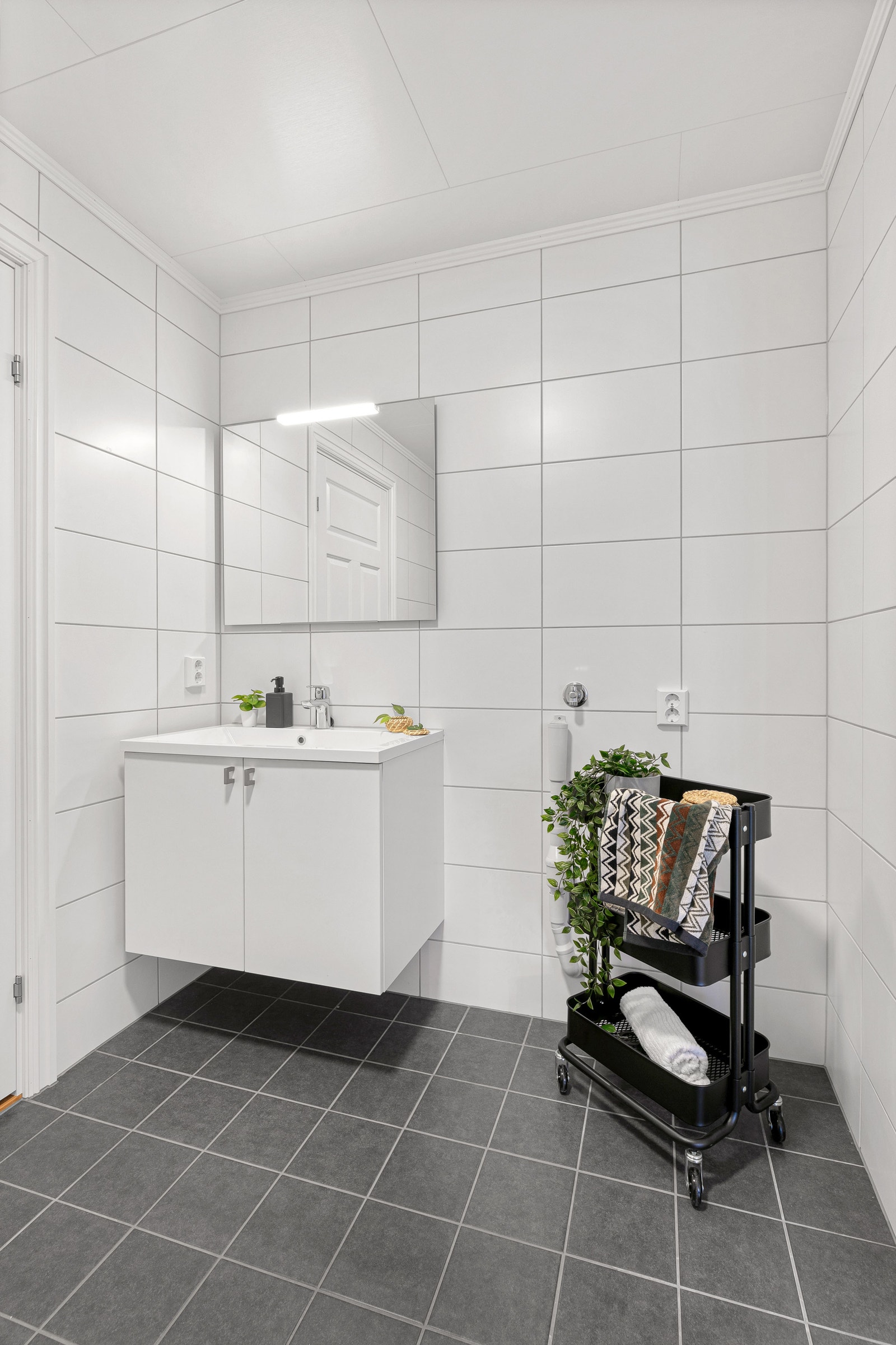 Bad med mørke fliser på gulv og lys innredning. Foto er fra annen leilighet med lik planløsning. Galleribilde