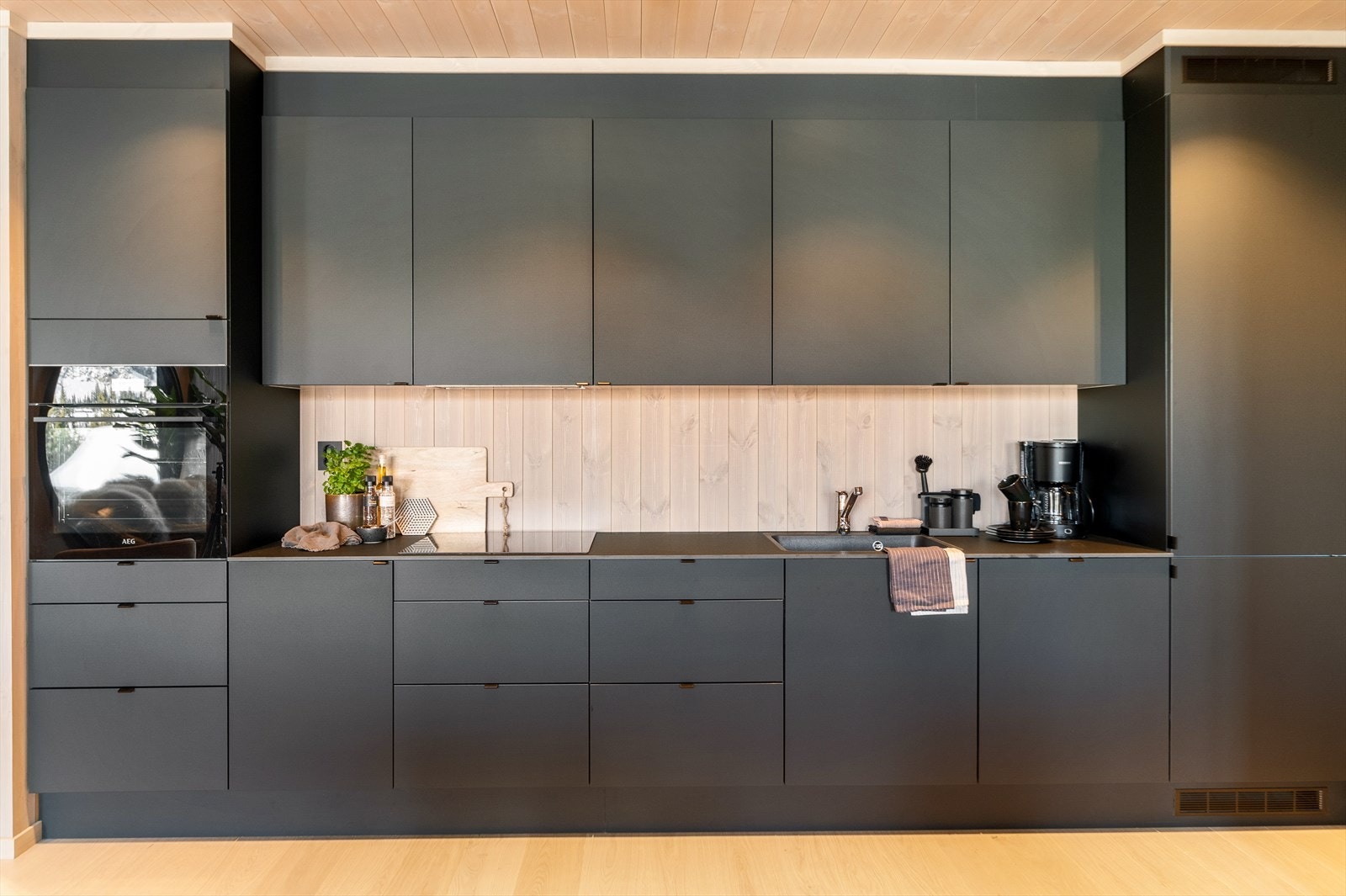 Integrerte hvitevarer som induksjonstopp, stekeovn, oppvaskmaskin og kombiskap medfølger med sorte detaljer fra AEG medfølger. Galleribilde