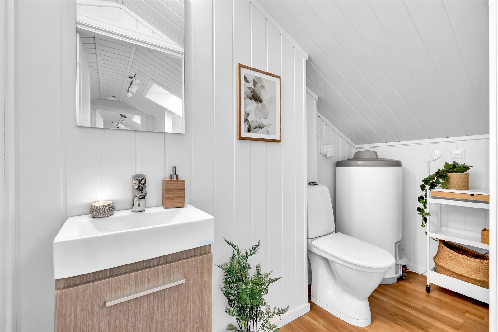 WC som er i loftetasjen har parkett på gulv samt hvitmalte panelplater. I rommet er det toalett, et servantskap og et speil med belysning. Galleribilde