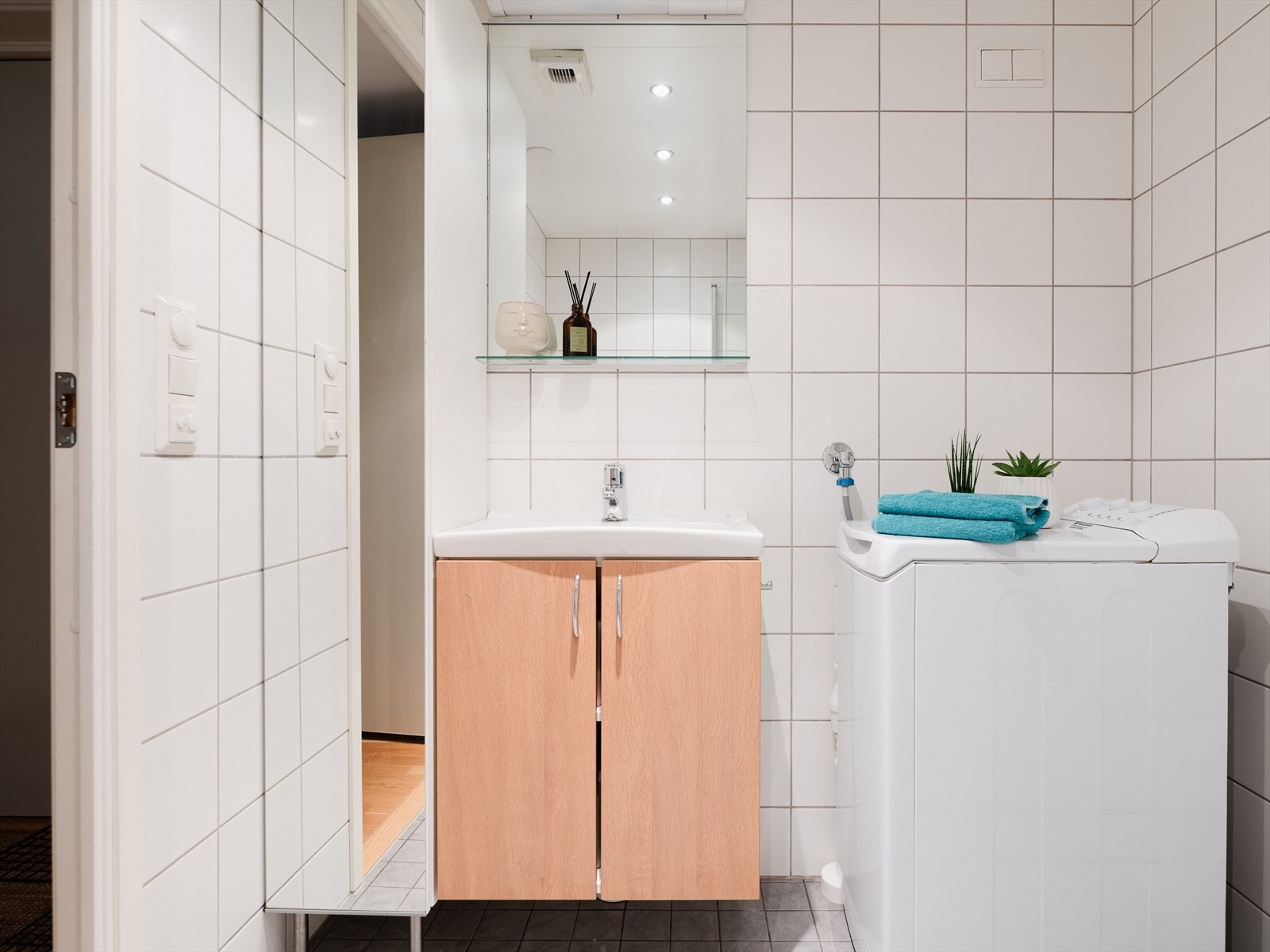 Badet er innredet med speil, servant på servantskap, vegghengt toalett, dusjhjørne og opplegg for vaskemaskin. Galleribilde