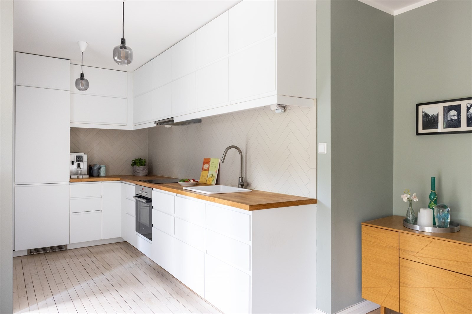 Innbydende og stilrent kjøkken med kjøkkeninnredningen bestående av hvite, glatte fronter og benkeplate av heltre med nedfelt vask. Galleribilde