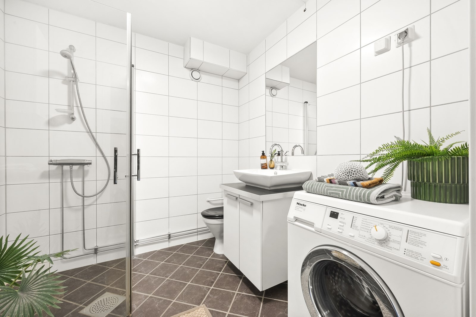 Badet er innredet med toalett, dusjhjørne med svingbare glassdører og baderomsinnredning med skap, servant og speil. Galleribilde