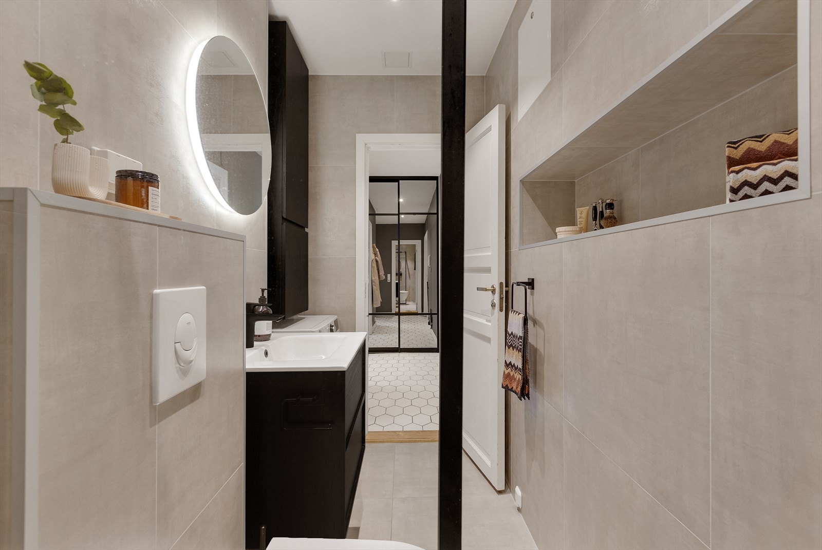 Badet har innredning med nedfelt servant, speil, veggmontert toalett, dusjvegger/hjørne og opplegg for vaskemaskin. Galleribilde