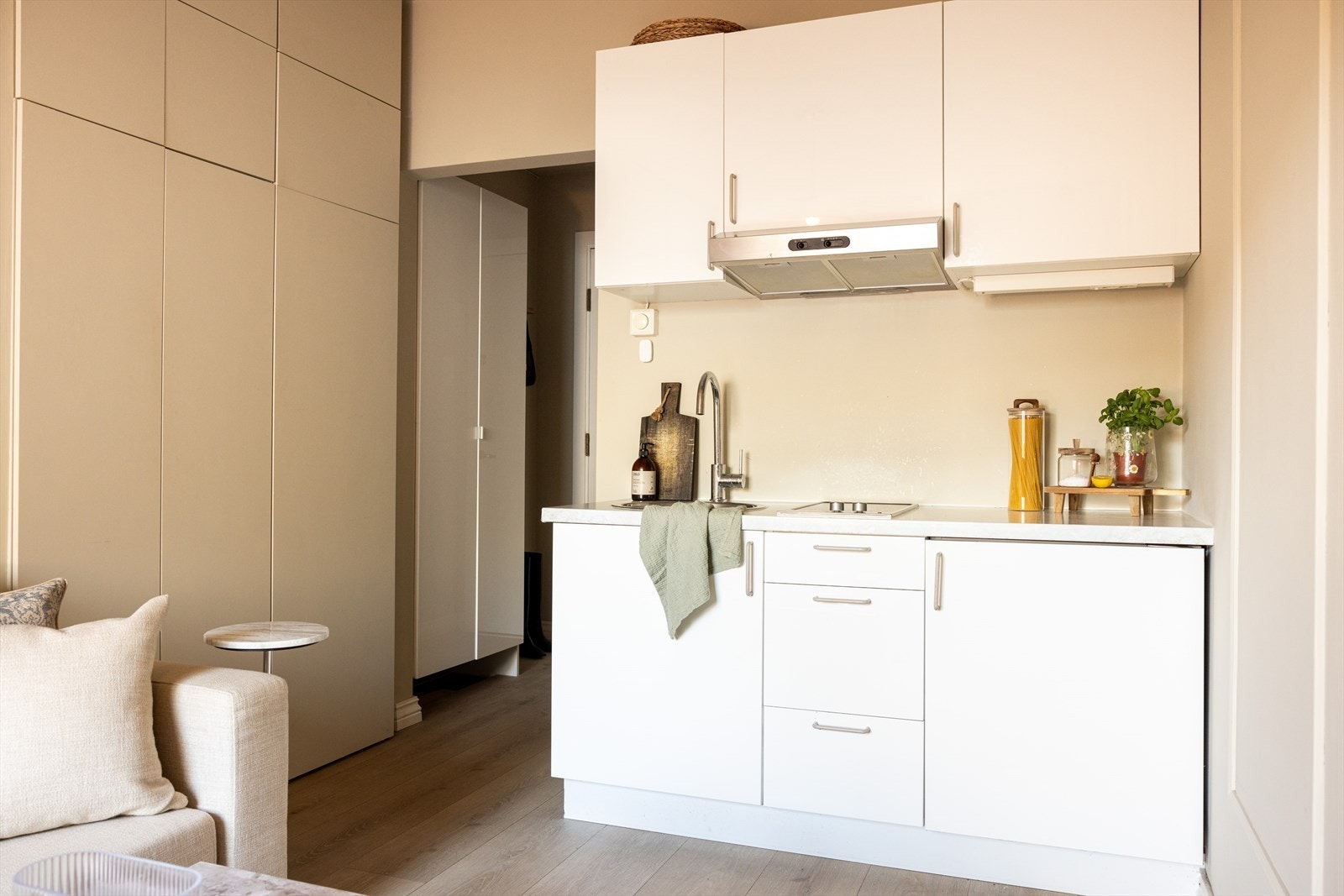 Stilrent kjøkken bestående av hvite, glatte fronter og benkeplate av laminat. Kjøkkenet er utstyrt med kjøleskap under benkeplate og platetopp. Galleribilde
