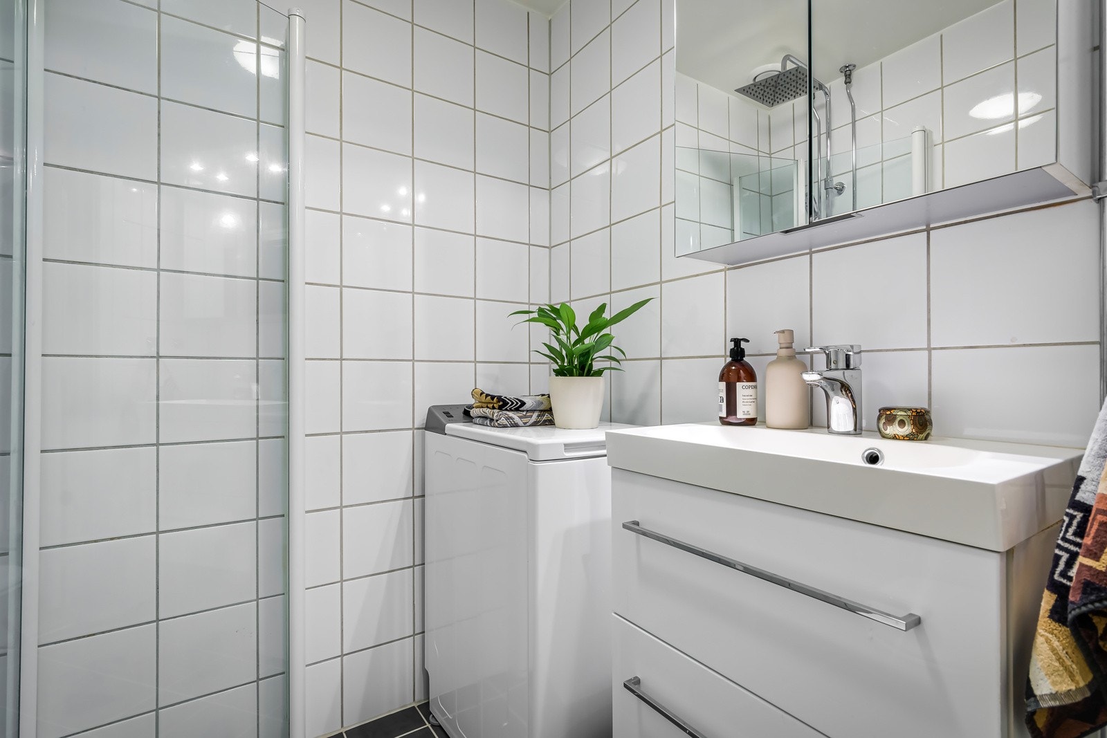 Baderommet har mørke fliser på gulv med gulvvarme, hvite fliser på veggene og nedsenket himling med malt flate. Galleribilde