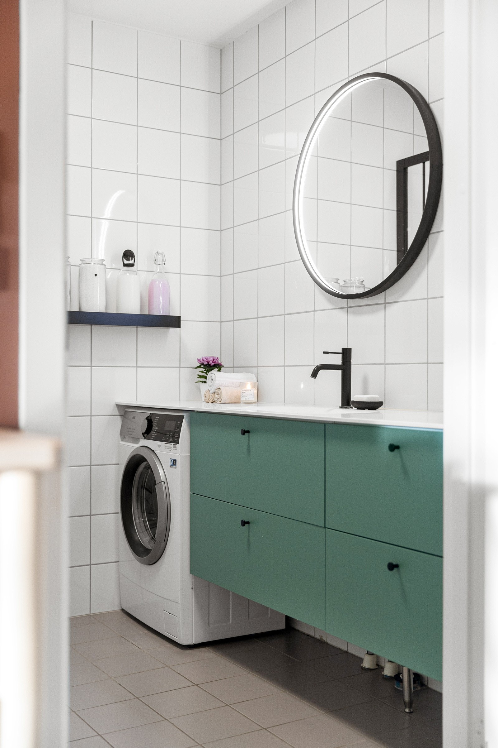 Baderomsinnredningen består av en seksjon med stor servantbenk og mørkegrønne skuffer, og under benken finnes opplegg for vaskemaskin Galleribilde