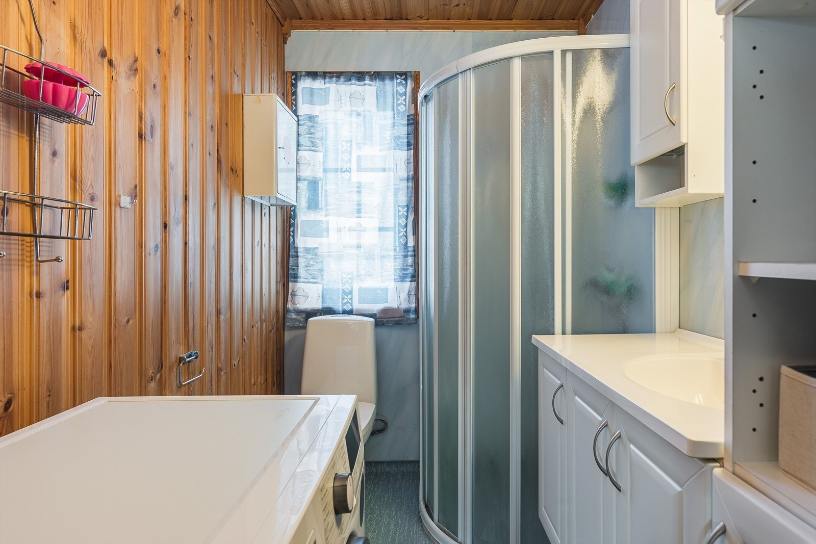 Badet er innredet med heldekkende servant nedfelt i benkeskap, overskap, dusjhjørne og frittstående toalett. Rommet varmes opp med panelovn og har opplegg for vaskemaskin. Galleribilde
