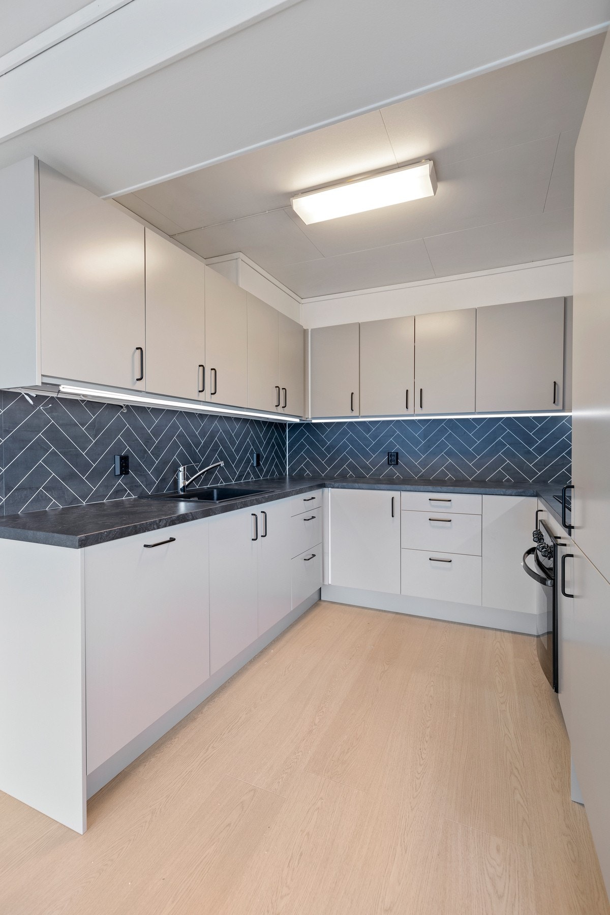 Benkeplaten er i laminat med nedfelt, sort servant, og det er montert kitchenboard i bakkant Galleribilde