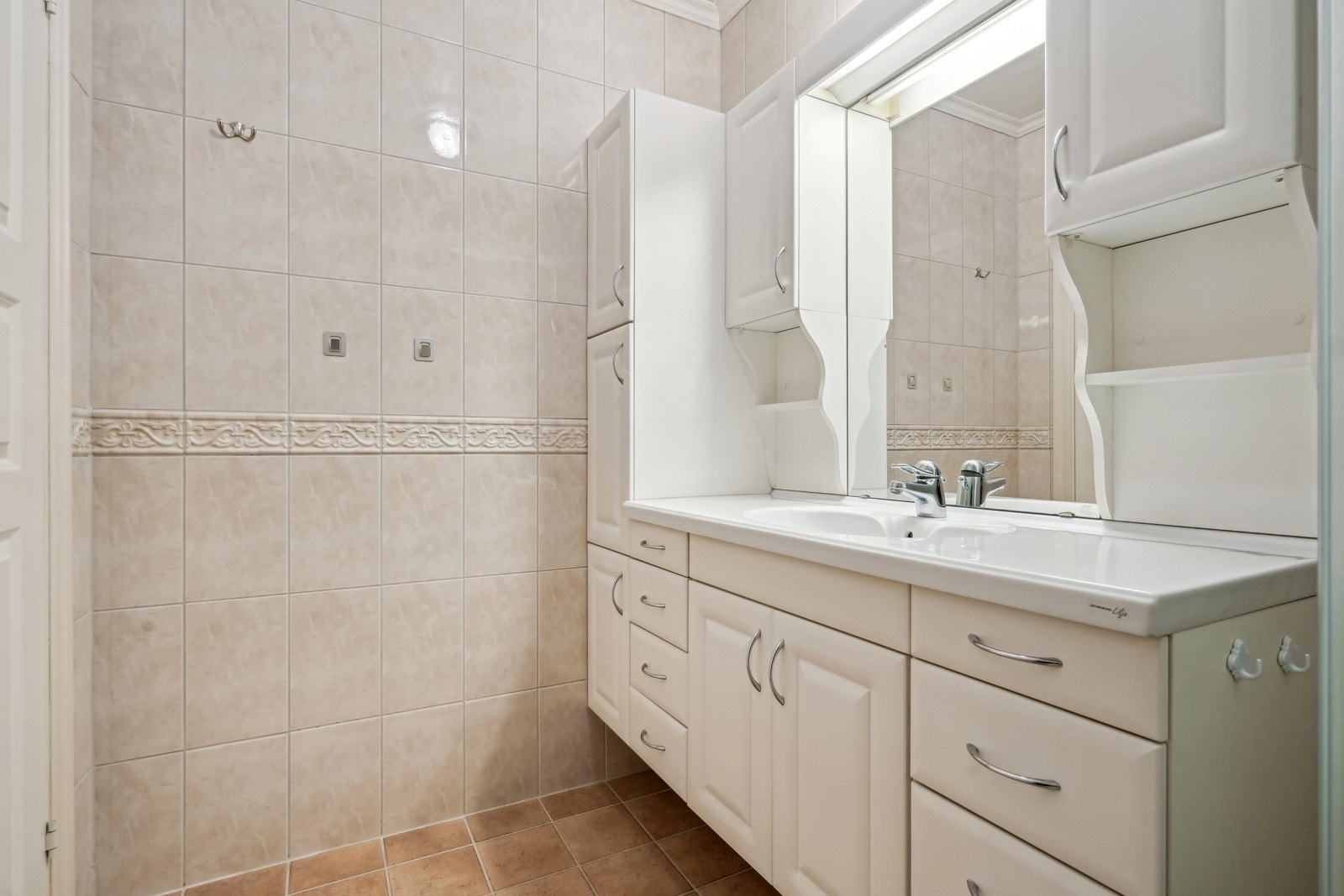 Badet har fliser på vegger og gulv med elektriske varmekabler. Stor baderomsinnredning med flere oppbevaringsskap, skuffer og speil med belysning over - Galleribilde