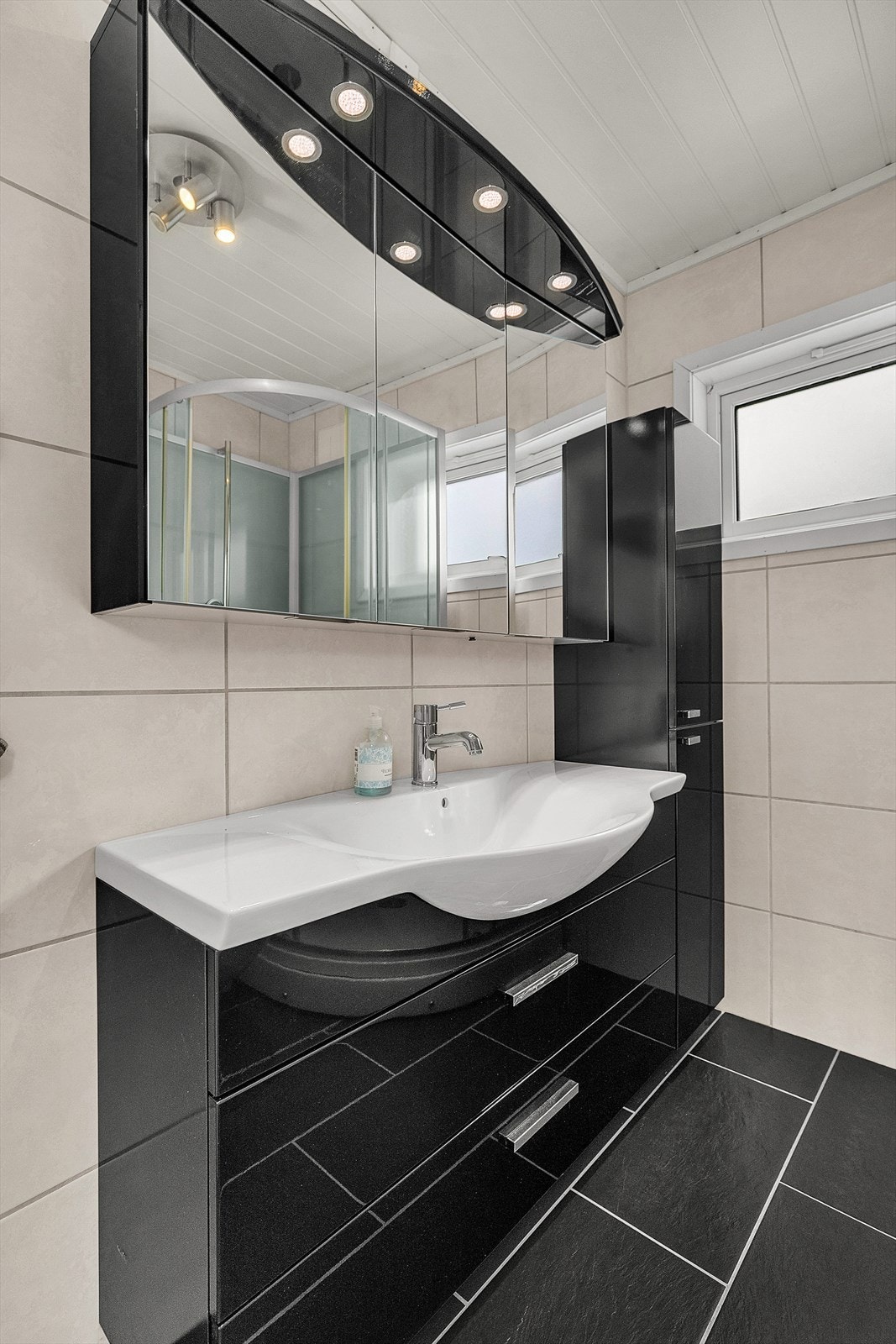 Flislagt bad med elektriske varmekabler i gulv. Romslig baderomsinnredning med sorte slette fronter. Galleribilde