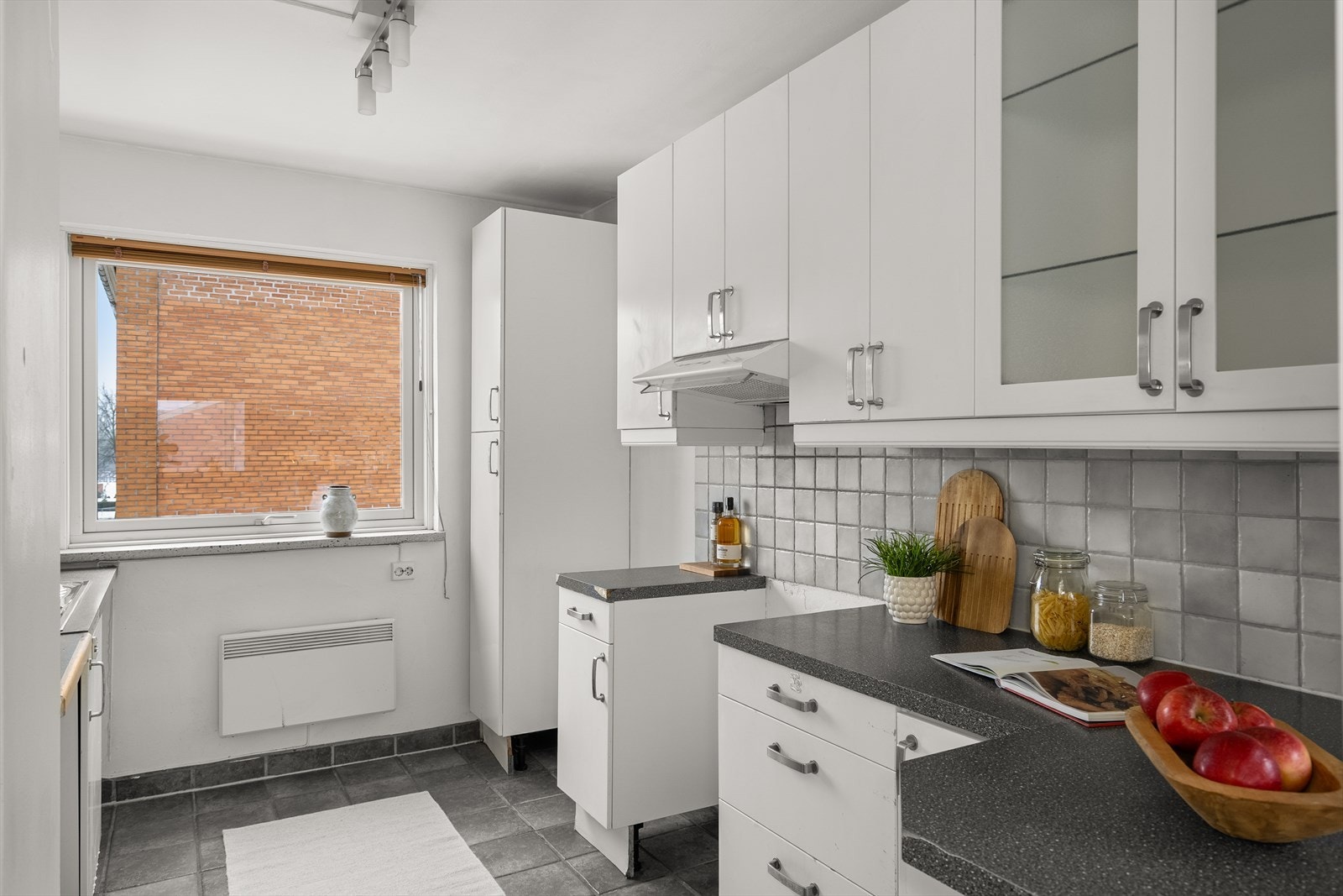 Boligens separate kjøkken er av eldre innredning med slette fronter, vitrineskap og laminat benkeplate. Fliser over benk. Nedfelt kum. Ett-greps kran. Ventilatorhette med kullfilter Galleribilde