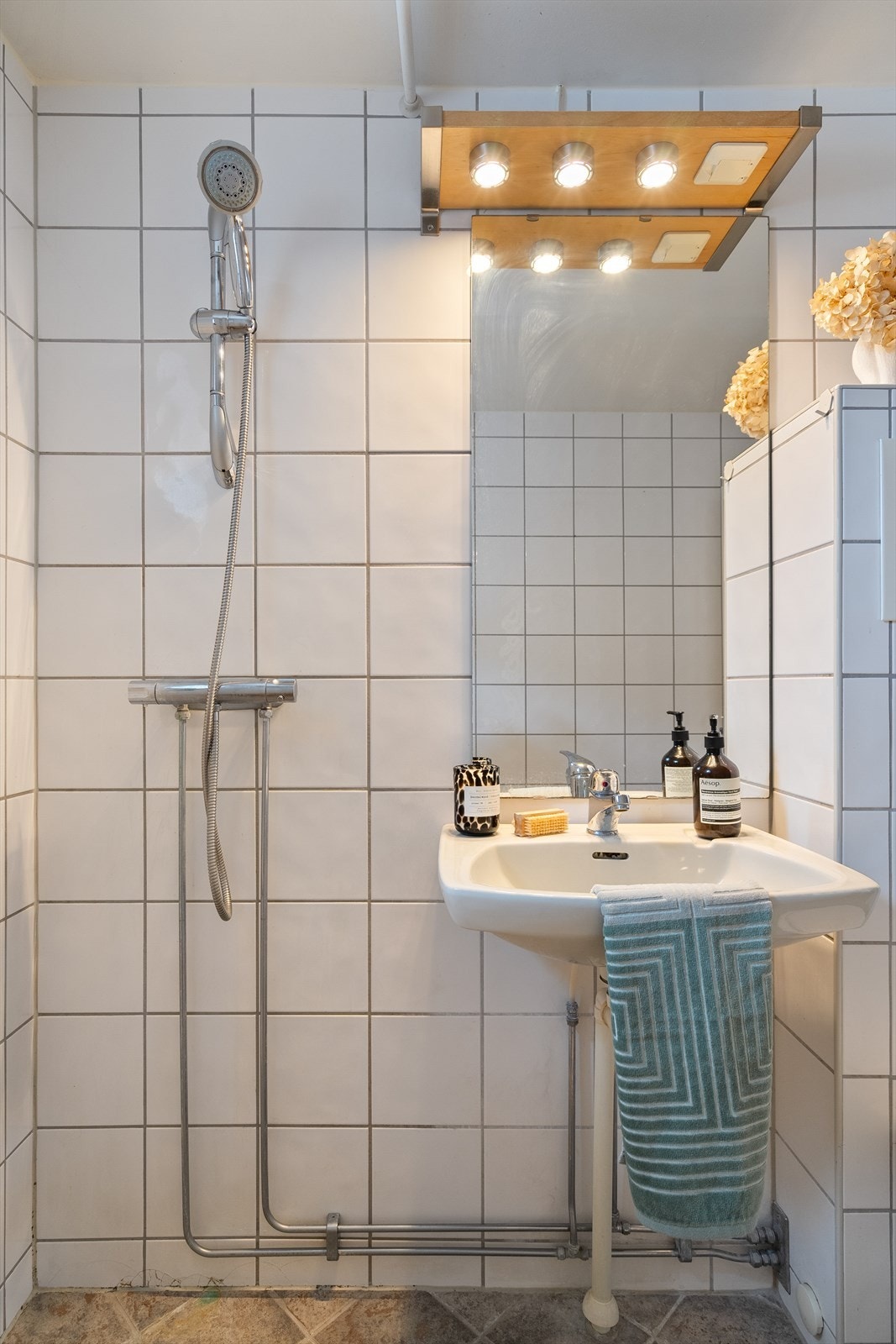 Badet består av vegghengt klosett, servant, ett-greps kran og dusjhjørne. Dusj direkte på gulvet. Speil med lys. Galleribilde