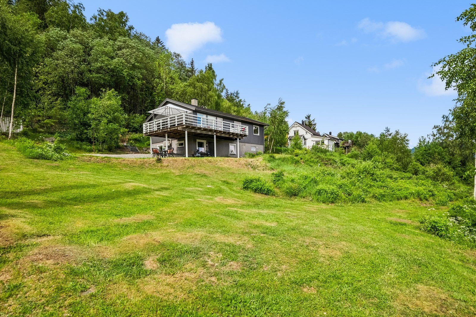 Tomten er pent opparbeidet med stort plenareal, busker og gruset innkjørsel. Galleribilde