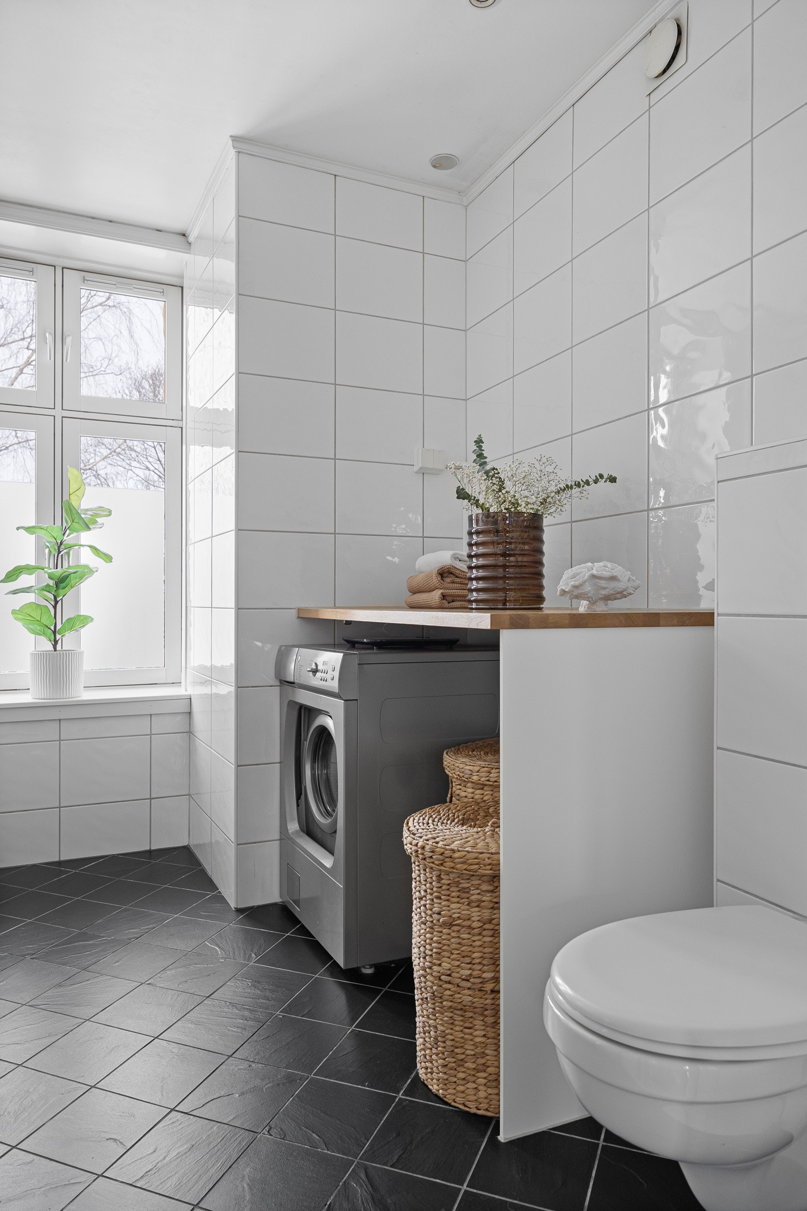 Dusjhjørne med innfellbare glassdører (dusjarmatur tilkoblet regndusj og hånddusj), vegghengt toalett, vegghengt servantinnredning med glatte fronter, heldekkende servant og speil på vegg over servant. Galleribilde