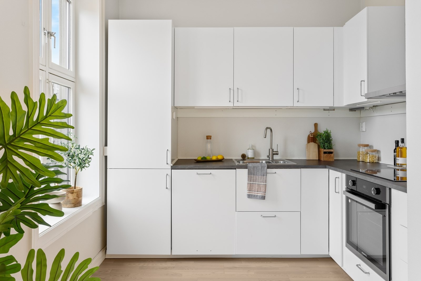 Lys kjøkkeninnredning fra 2022. Laminat benkeplate med nedfelt vask. Integrert platetopp og stekeovn. Galleribilde