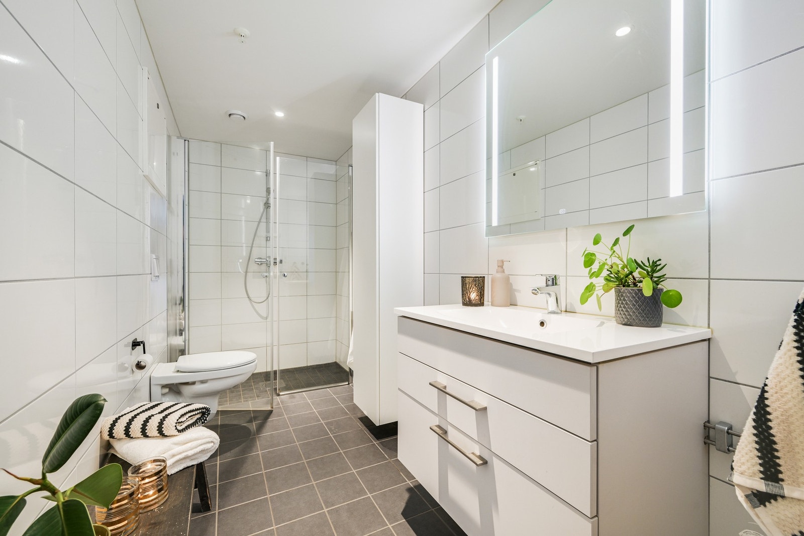 En-suite baderom. Et lyst og moderne bad med flislagte vegger og gulv. Rommet har dusjkabinett, vegghengt toalett og servant med skuffer. Galleribilde