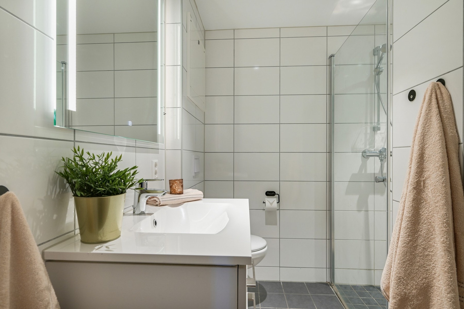 Bad nr. 3 med flislagte vegger og gulv, klosett, servant med speilskap og belysning, samt dusjhjørne med glassvegg. Galleribilde