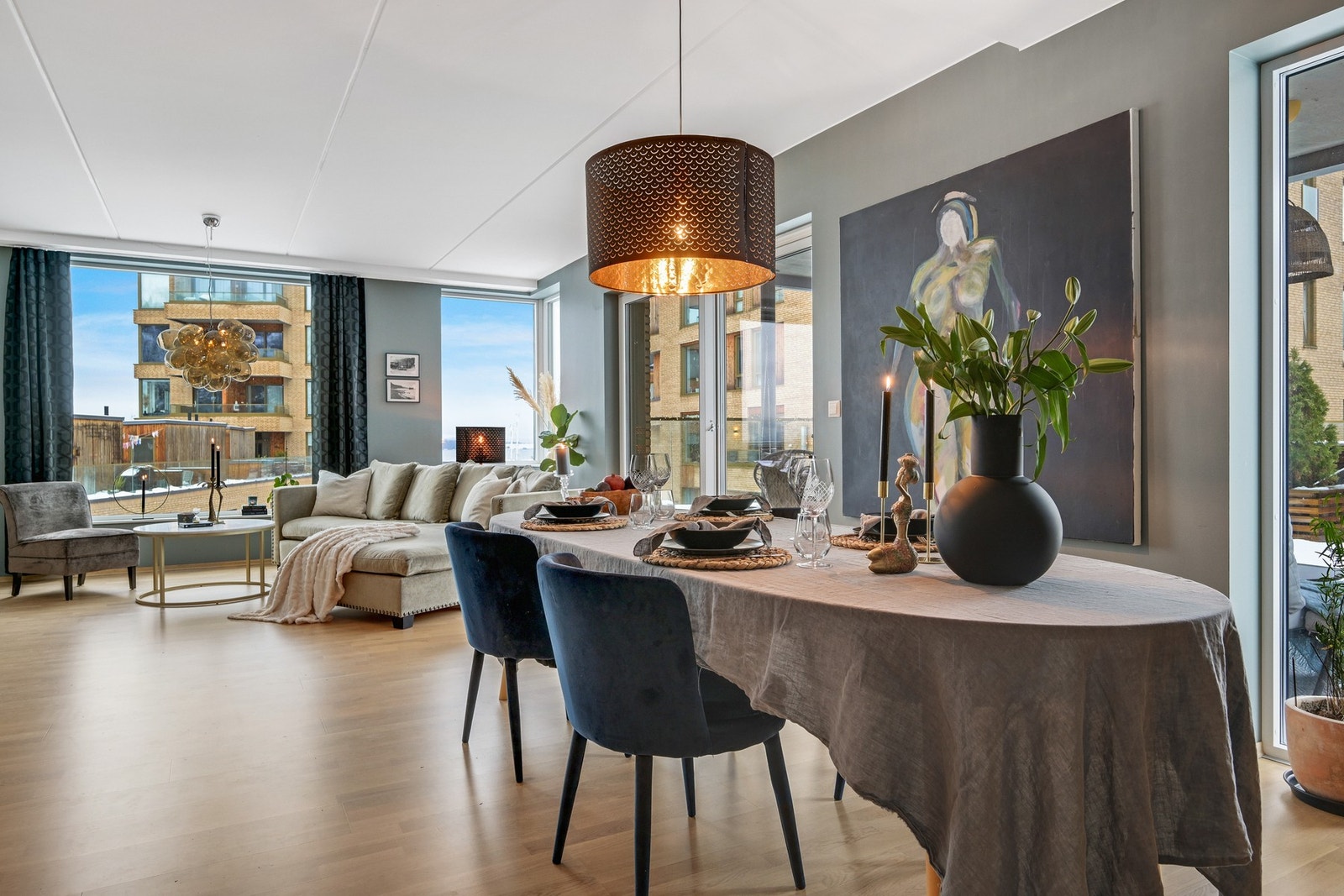 Lys og romslig stue med store vindusflater og åpen løsning mot spiseplass. Moderne interiør med lys parkett og nøytrale veggfarger. Galleribilde