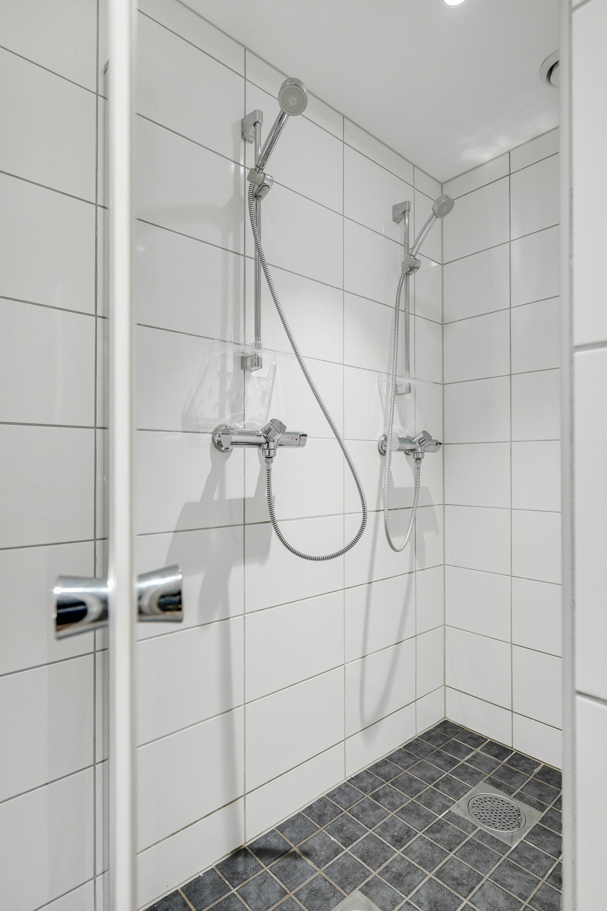 Dusjhjørne med flislagte vegger og gulv, samt to dusjhoder. Galleribilde