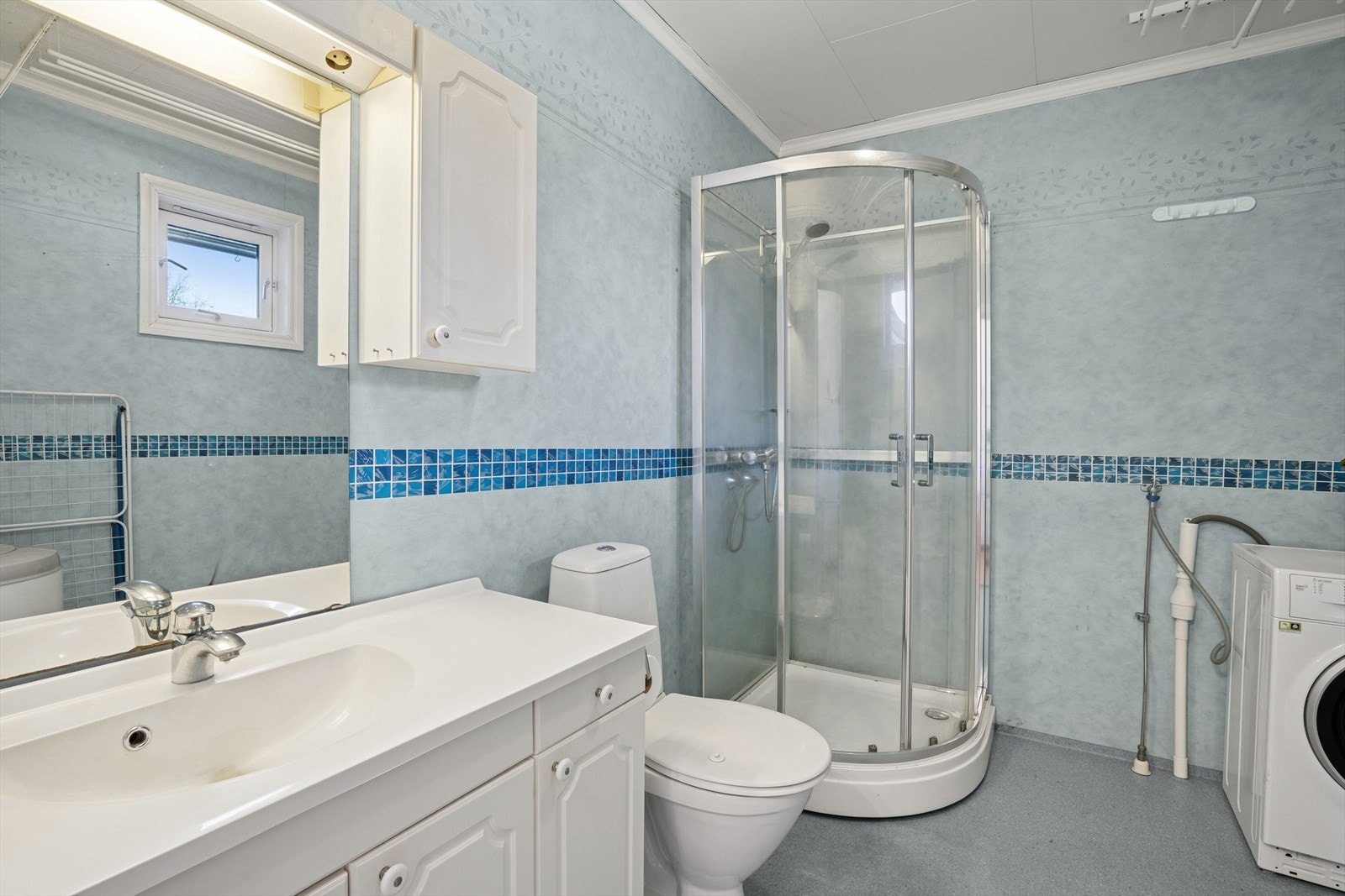 Badet er innredet med toalett, dusjkabinett, innredning med servant og opplegg til vaskemaskin. Galleribilde
