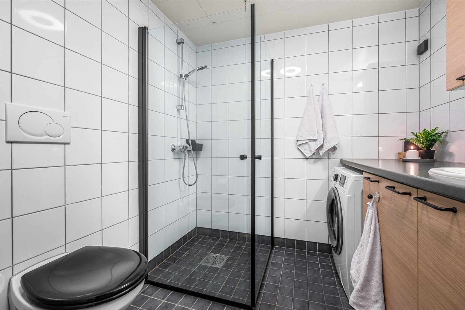 Baderommet består av dusjnisje med dusjgarnityr på vegg, opplegg for vaskemaskin, innredning med servant og vegghengt toalett. Galleribilde