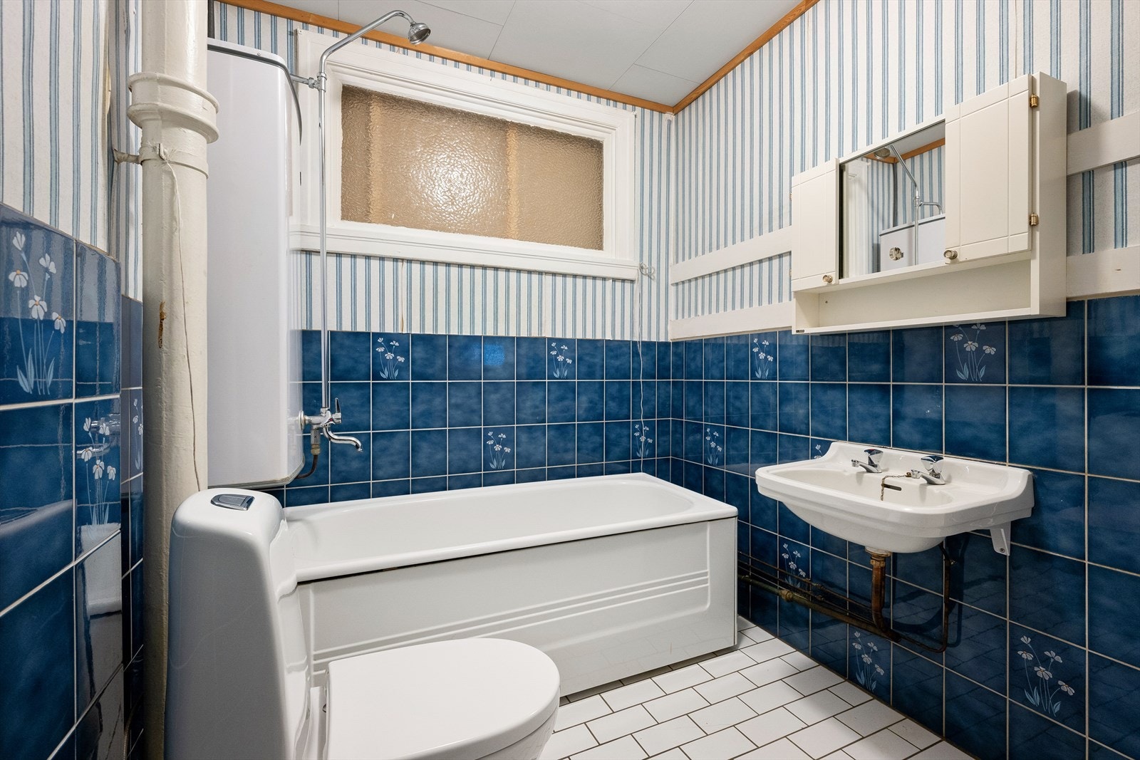 Baderom av eldre dato, innredet med dusj i badekar, servant og gulvstående klosett Galleribilde