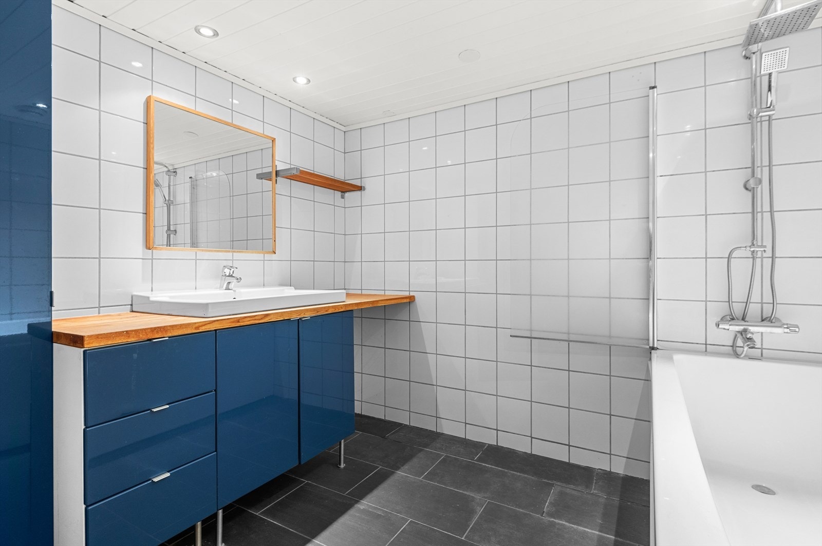 Badet er flislagt fra topp til tå, det er utstyrt med badekar, opplegg for vaskemaskin, servant, servantskap og veggmontert wc. Galleribilde