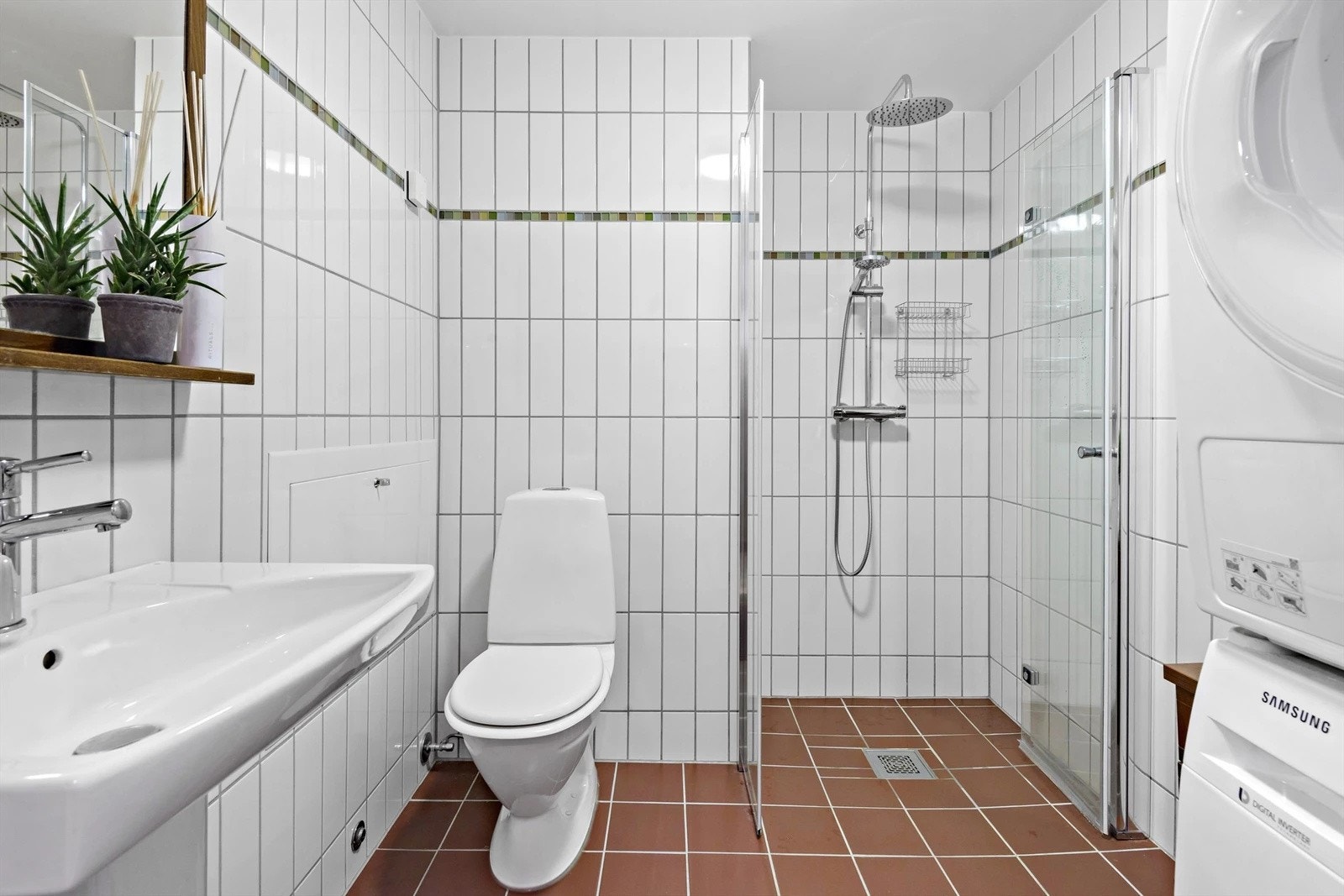 Flislagt baderom utstyrt med vegghengt servant, speil, toalett og dusjnisje med både hånddusj og regndusj. Det er også opplegg for vaskemaskin. Galleribilde