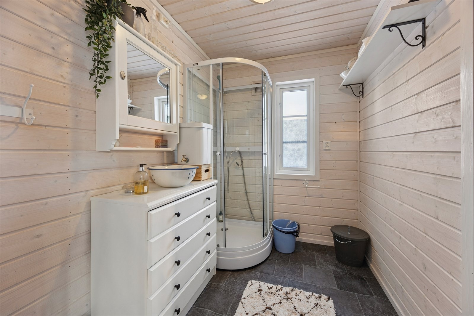 Baderommet har belegg på gulv og panel på vegg og himling. Rommet har ikke fast vann
innstallsjon. Det er ikke sluk i gulvet til avløp fra dusj, eier opplyser at det er boret hull gjennom gulvet for
og slippe ut gråvann. Galleribilde