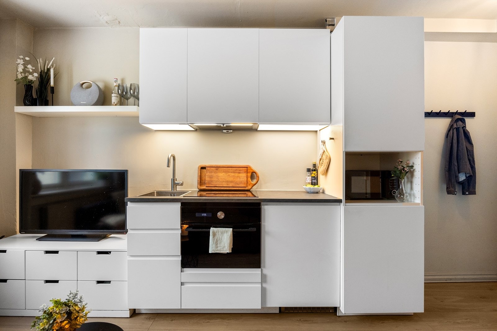 Moderne kjøkkeninnredning fra 2019 med hvite, laminerte fronter, kullfiltervifte over integrert koketopp og ovn, laminert benkeplate, samt integrert kjøleskap. Galleribilde