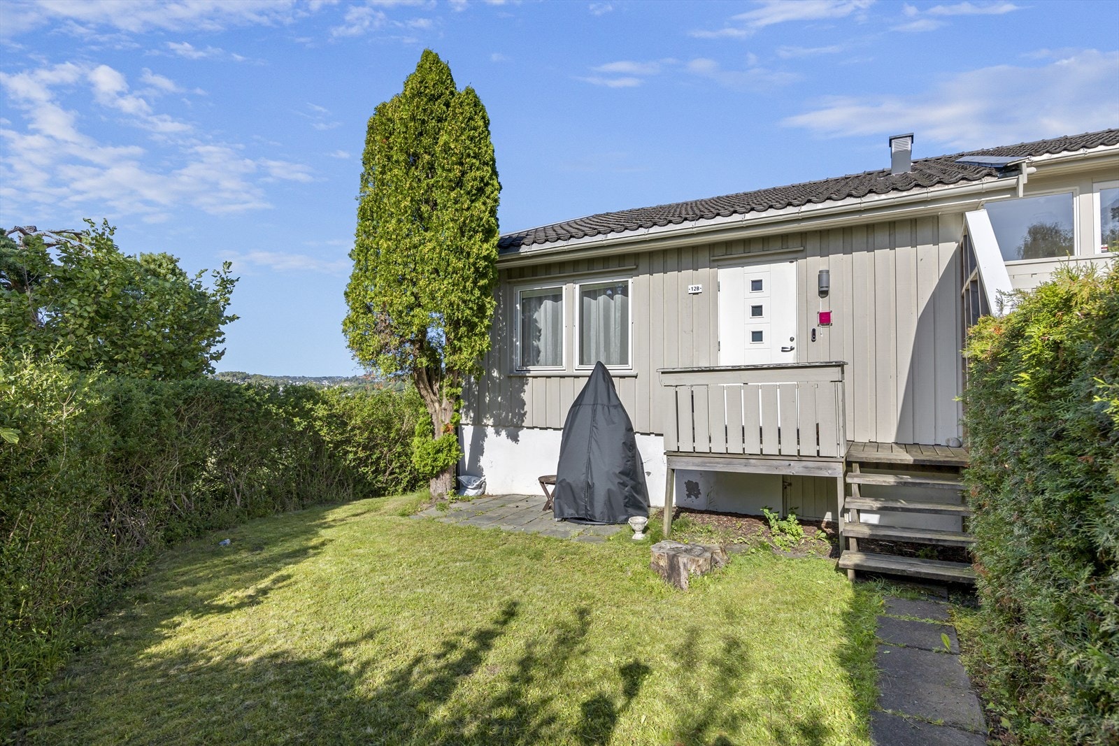 Inngang til leiligheten med tilhørende uteplass. Leiligheten inneholder bl.a. stue med åpen kjøkkenløsning, to soverom og bad/vaskerom Galleribilde