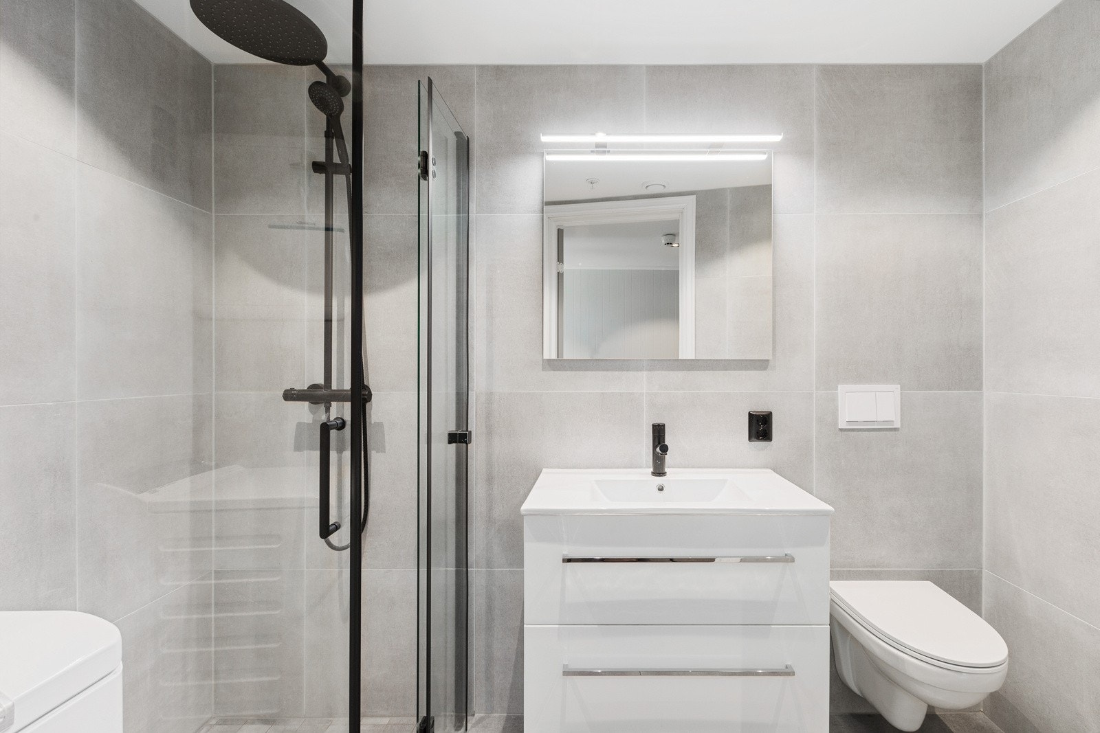 Flislagt bad med opplegg for vaskemaskin. Dusjdører i glass, vegghengt klosett og varmekabler i gulv. Galleribilde