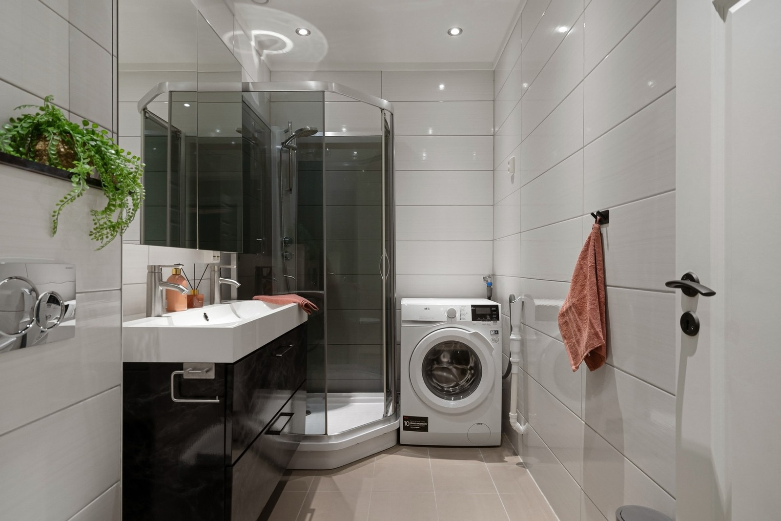 Lekkert, flislagt bad med nedfelt servant med 2 kraner, veggmontert toalett, dusjkabinett og opplegg for vaskemaskin. Galleribilde