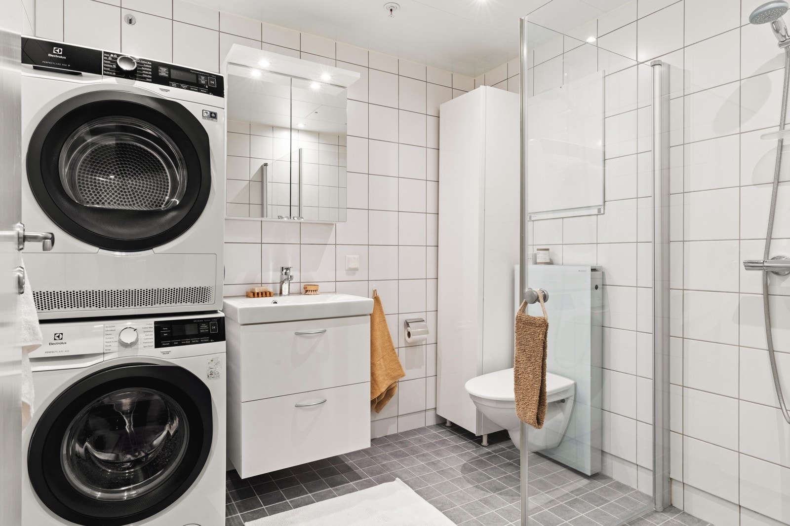 Badet er innredet med vegghengt toalett, dusj med glassdører, opplegg for vaskemaskin og baderomsinnredning. Galleribilde