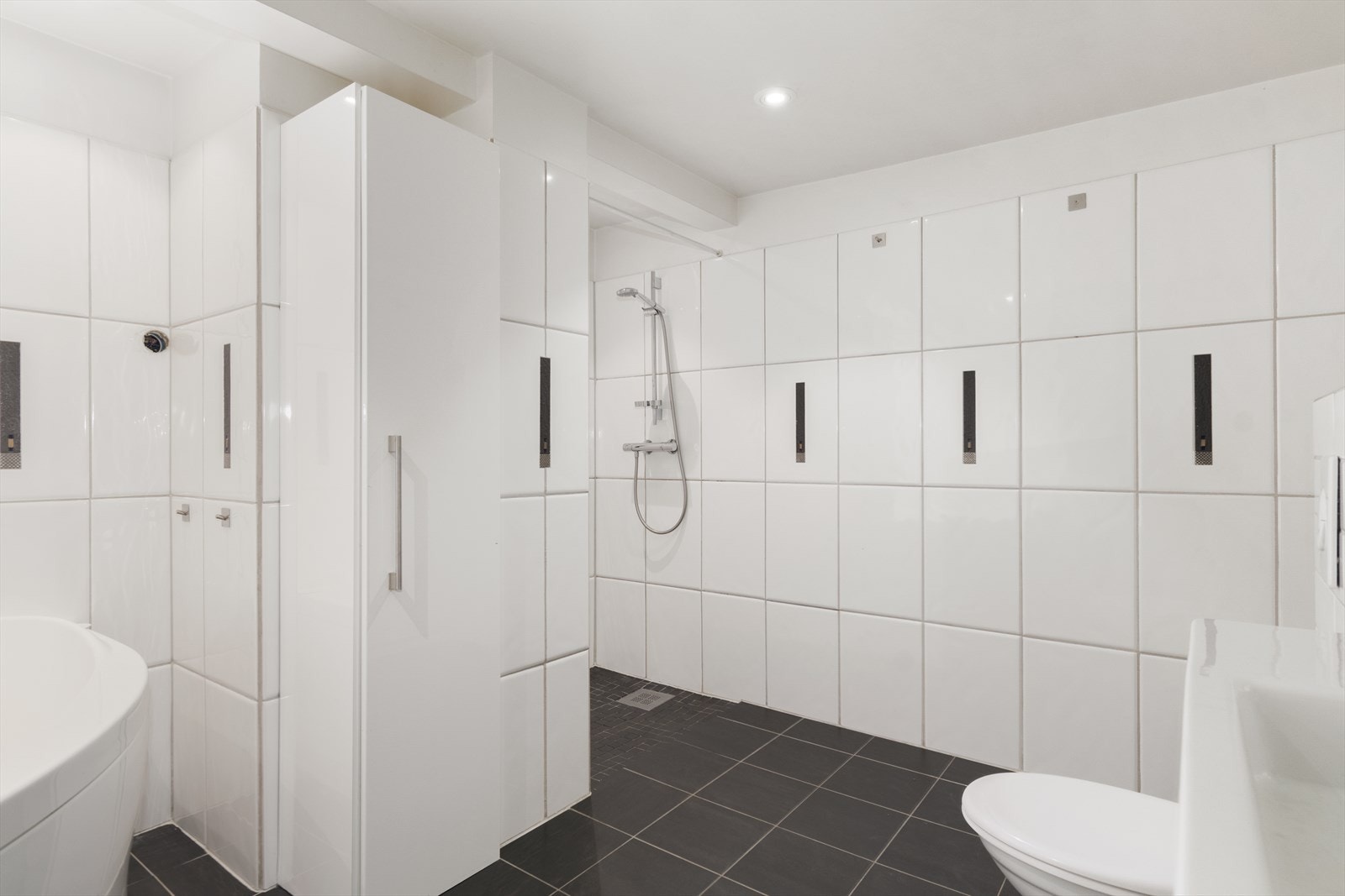 Badet har både badekar og dusjnisje. Toalett, veggskap samt servant med skuffer. Downlights i himling Galleribilde